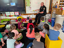 Officer reading a book to students in a classroom